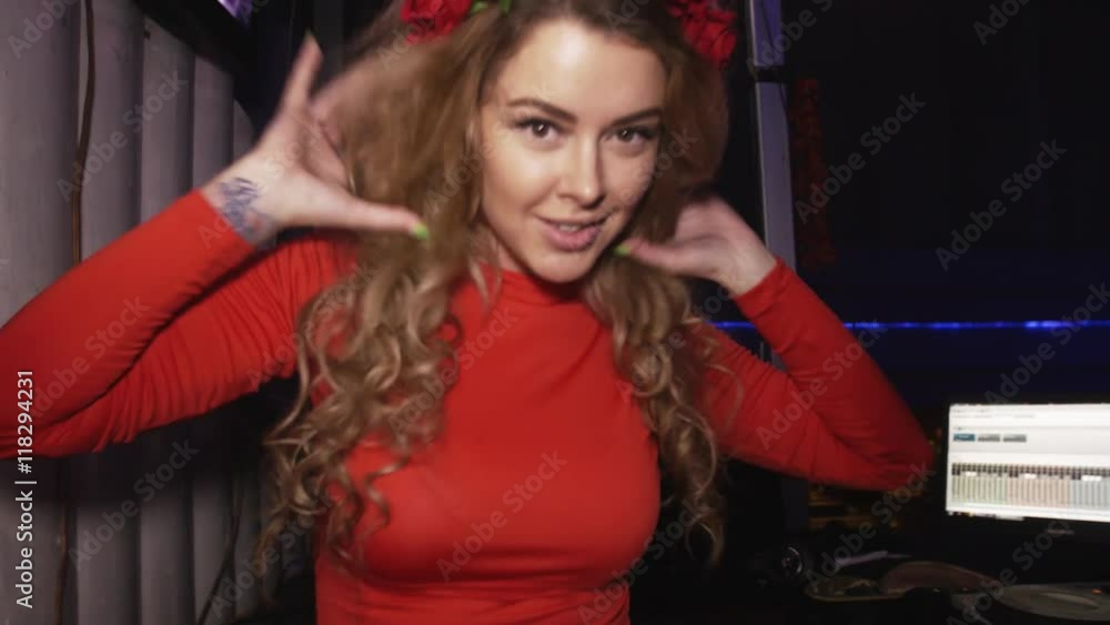 Dj girl in red dress dancing at turntable in nightclub. Hands movements. Red rim on head Dj girl in red dress dancing at turntable in nightclub. Hands movements. Red rim on head