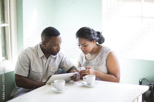 Smiling couple using cell phone and digital tablet at breakfast