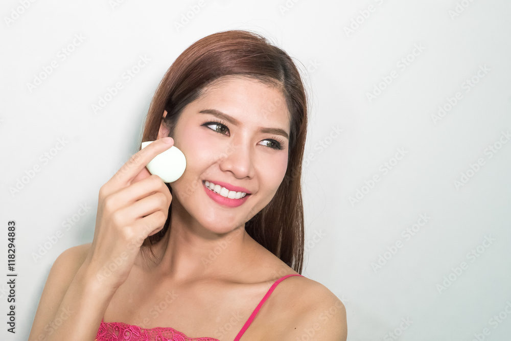 Beautiful young woman applying foundation to face with green egg Beautiful young woman applying foundation to face with green egg
