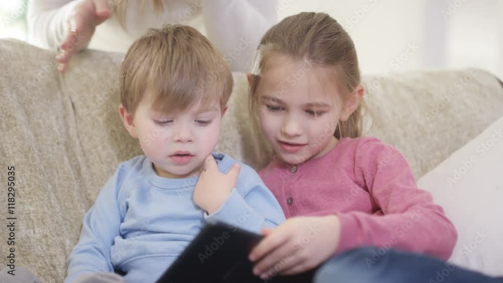 Cute little boy & girl looking at tablet computer as mother watches over them Cute little boy & girl looking at tablet computer as mother watches over them