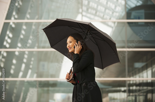 Smiling businesswoman with umbrella talking on cell phone photo