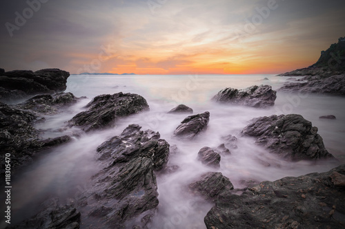 Soft waves of ocean in sunset with stones on the beach foregroun