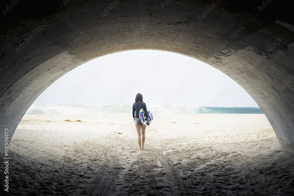© Alberto Guglielmi/Blend Images - Caucasian woman carrying skimboard under arch © Alberto Guglielmi/Blend Images - Caucasian woman carrying skimboard under arch