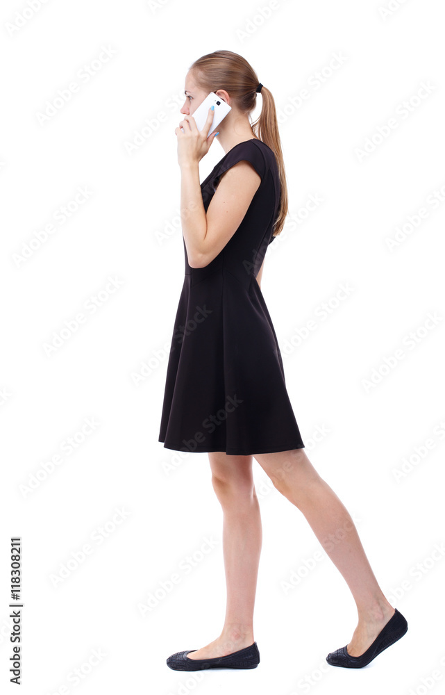 side view of a woman walking with a mobile phone. back view of girl in motion. backside view of person. Rear view people collection. Isolated over white background. Blonde in a short black dress is side view of a woman walking with a mobile phone. back view of girl in motion. backside view of person. Rear view people collection. Isolated over white background. Blonde in a short black dress is