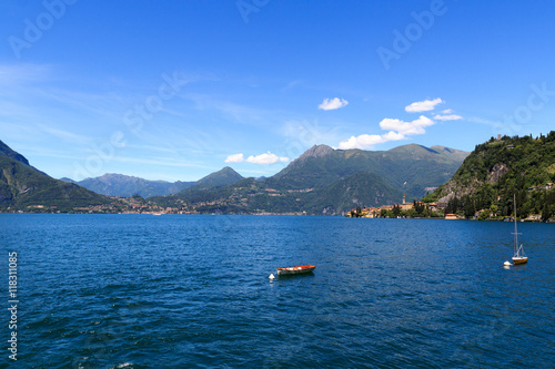 View towards Lake Como with boats and village Varenna with mountains in Lombardy, Italy