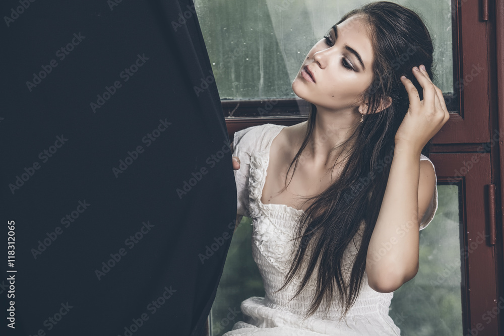 Beautiful young girl in jeans and top posing in a large window w Beautiful young girl in jeans and top posing in a large window w