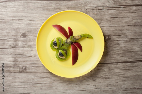 Dragonfly made of apple and kiwi on plate and desk