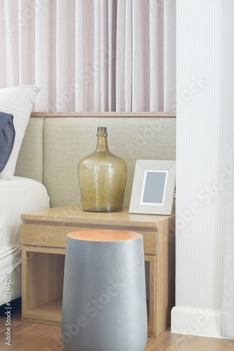 Round shape wooden stool next to bedside table in bedroom