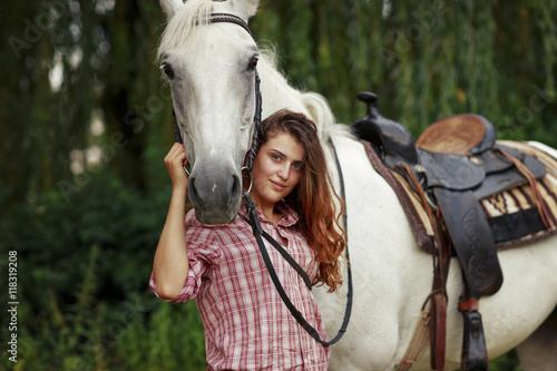 Beautiful girl near the horse. Ginger hair girl in checkered shirt with white horse.