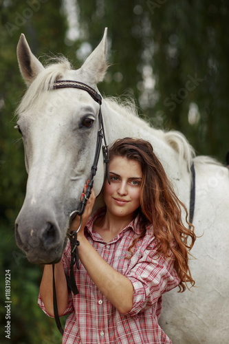 Beautiful girl near the horse. Ginger hair girl in checkered shirt with white horse.