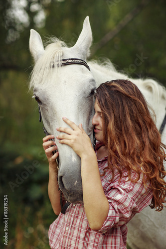 Beautiful girl near the horse. Ginger hair girl in checkered shirt with white horse. © oksanazahray