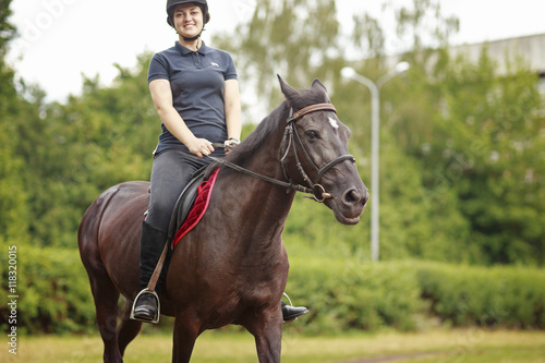 Girl riding a horse. Girl in dark helmet, jeans and high boots on a brown horse