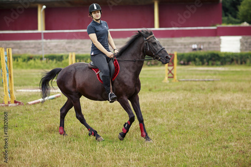 Girl riding a horse. Girl in dark helmet, jeans and high boots on a brown horse