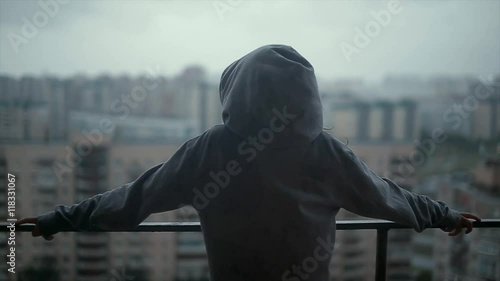 Girl in a hoodie on the balcony and looking at the high-rise buildings. It's raining.