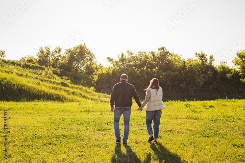 Couple walking in autumn sunset countryside meadow holding hands © satura_