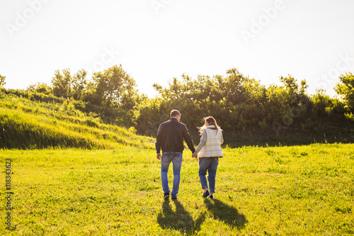 Couple walking in autumn sunset countryside meadow holding hands