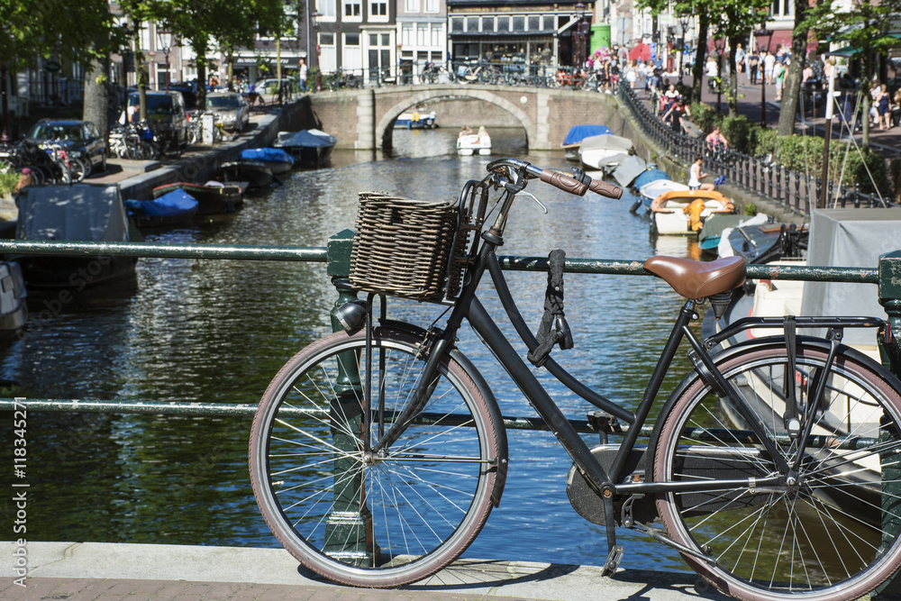 One bike with basket on the pavement near the bridge over the canal in the sunlight in Amsterdam