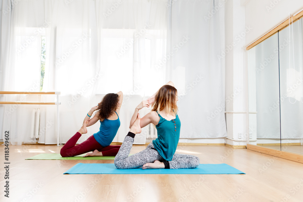 Side view portrait of two young women practice pigeon pose Side view portrait of two young women practice pigeon pose