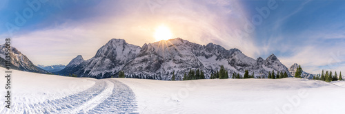 Sunny winter day in the mountains - Alpine panorama with the Austrian Alps mountains, the green trees and a thick layer of snow over its pastures. A gorgeous sun overwhelms the entire scene. © YesPhotographers