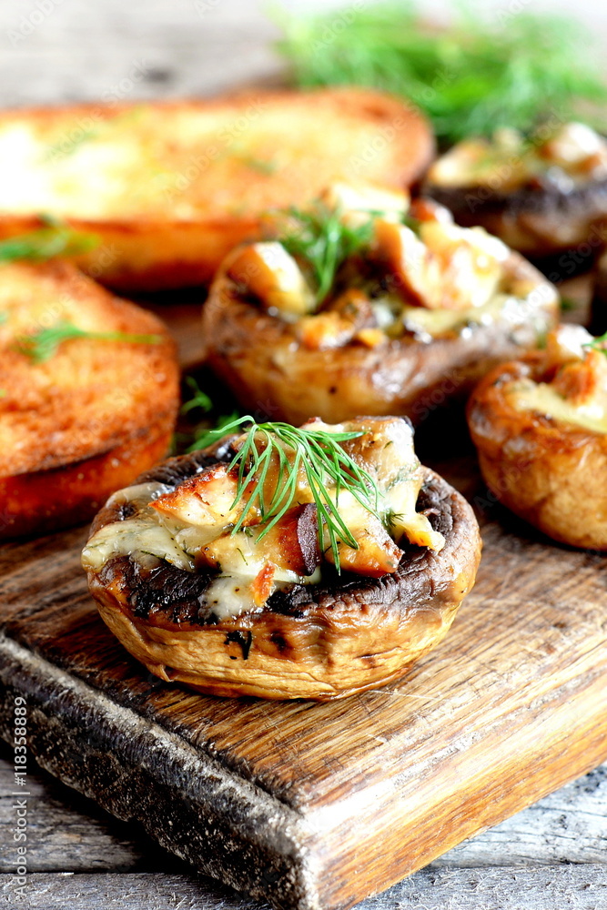 Stuffed mushrooms and fried toasts on a chopping board and wooden table. Baked mushroom caps stuffed with cheese and meat recipe. Closeup