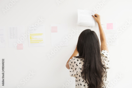 Businesswoman taping up papers on office wall photo