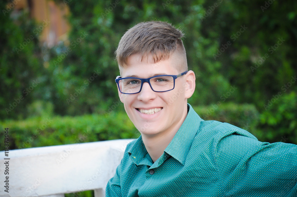 Attractive happy expression smiling american student man with glasses posing evening on the street in the summer. Outdoor closeup hipster portrait. Attractive happy expression smiling american student man with glasses posing evening on the street in the summer. Outdoor closeup hipster portrait.