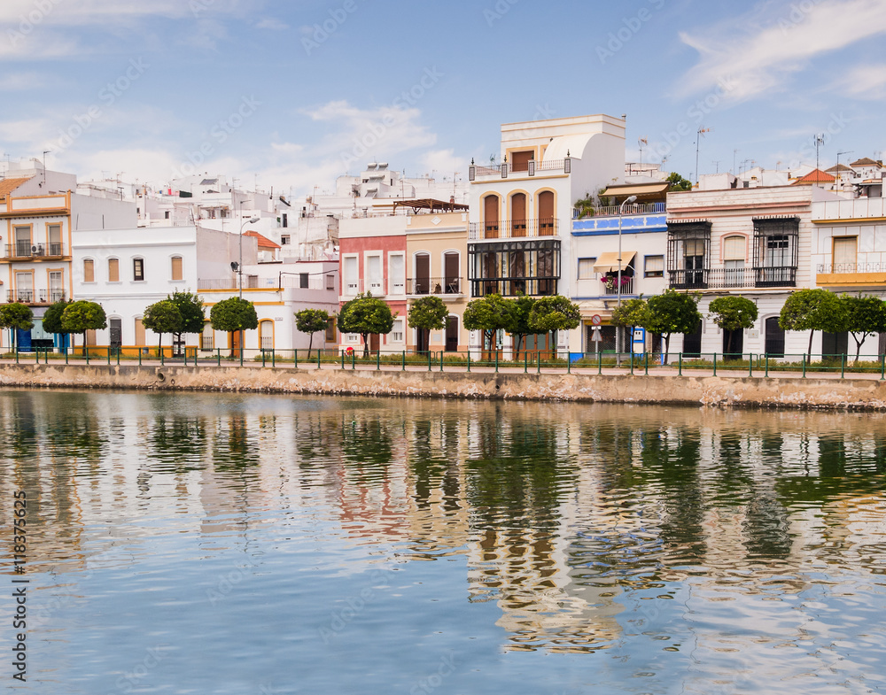 Traditional white architecture of the region along the riverbank in Ayamonte, Huelva province, Andalucia, Spain.  The buildings and clouds are reflecting in the river. - obrazy, fototapety, plakaty 