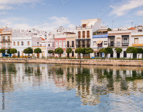 Traditional white architecture of the region along the riverbank in Ayamonte, Huelva province, Andalucia, Spain. The buildings and clouds are reflecting in the river.