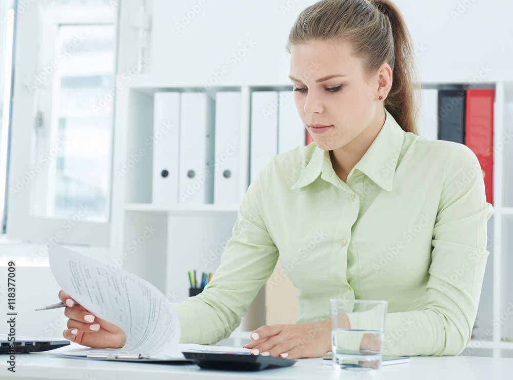 Beautiful young secretary .viewing entries in the papers on the clipboard sitting at office. Beautiful young secretary .viewing entries in the papers on the clipboard sitting at office.