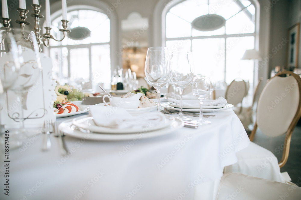 Elegant wedding reception white table arrangement restaurant, candlestick on table. Plates, forks and glasses