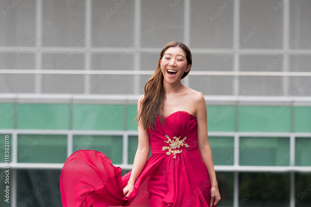 Happy and smiling cute Asian woman walking in red evening dress