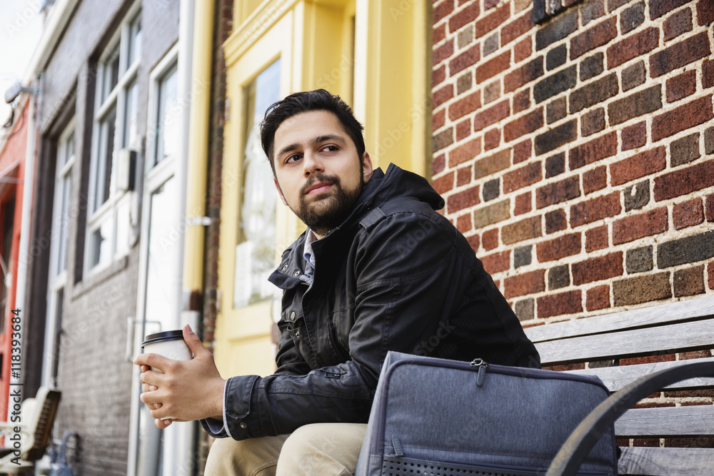 Hispanic man sitting on city bench drinking coffee Hispanic man sitting on city bench drinking coffee