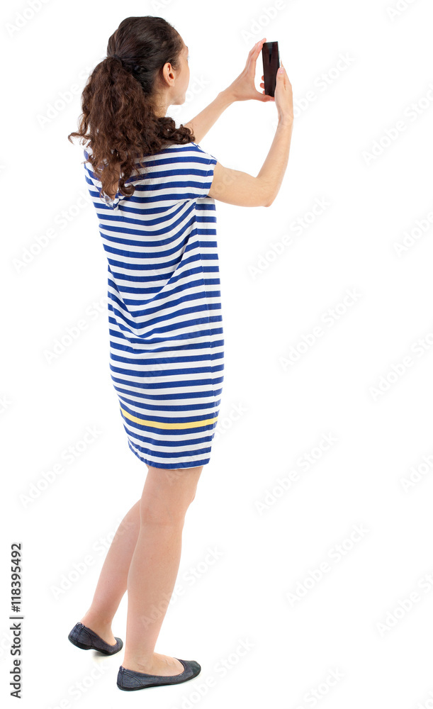 back view of standing young beautiful woman using a mobile phone. girl watching. Rear view people collection. backside view of person. Isolated over white background. Swarthy girl in a checkered back view of standing young beautiful woman using a mobile phone. girl watching. Rear view people collection. backside view of person. Isolated over white background. Swarthy girl in a checkered