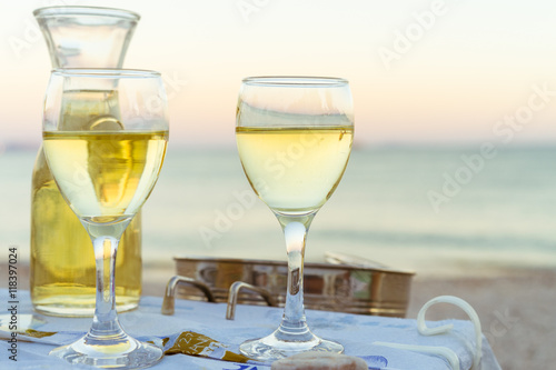 The carafe of white wine and a glass of wine on the beach, sunset, dinner by the sea, holiday, romance. Holidays in Greek wine in Greece.