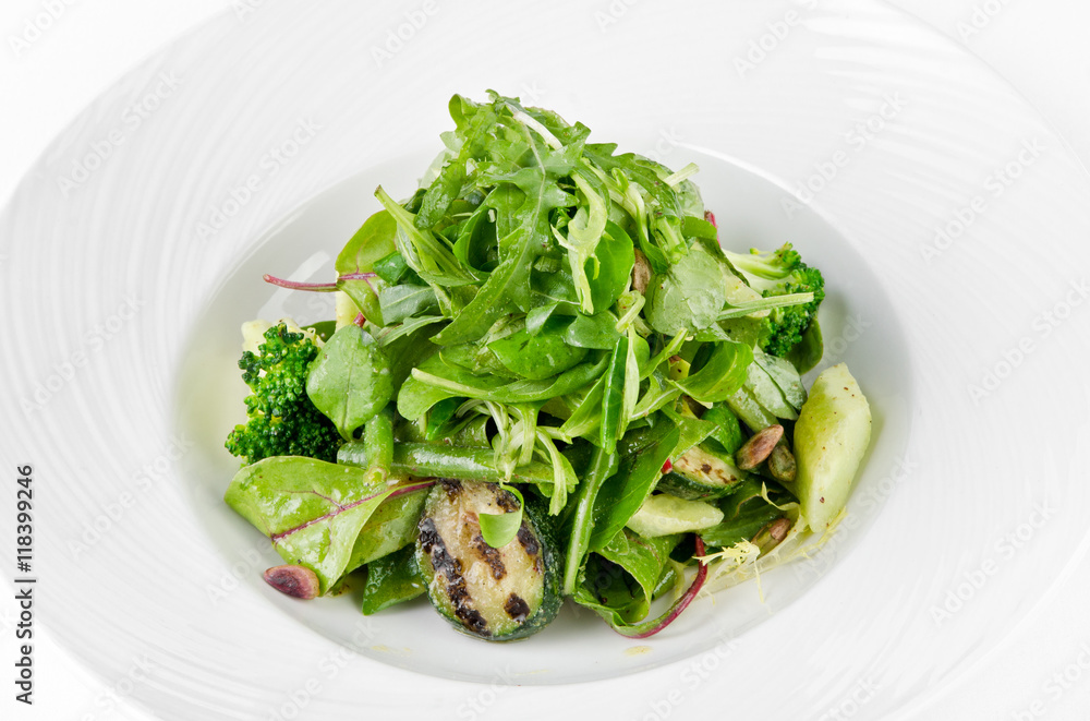 Salad of green vegetables with broccoli, zucchini and walnut dressing on a plate on a white background, closeup