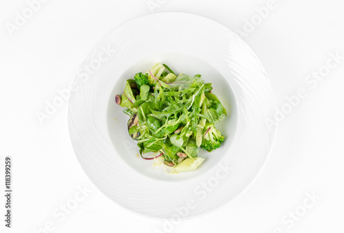 Salad of green vegetables with broccoli, zucchini and walnut dressing on a plate on a white background, top view