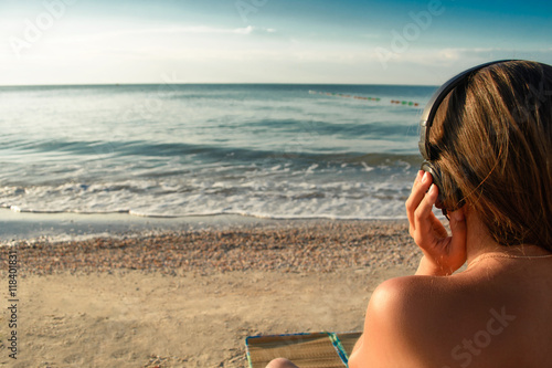 Beautiful young girl in bikini is listening music with headphones on the beach