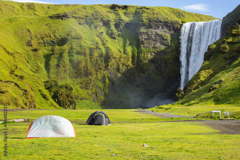 tourist tents before big waterfall in green valley in Iceland