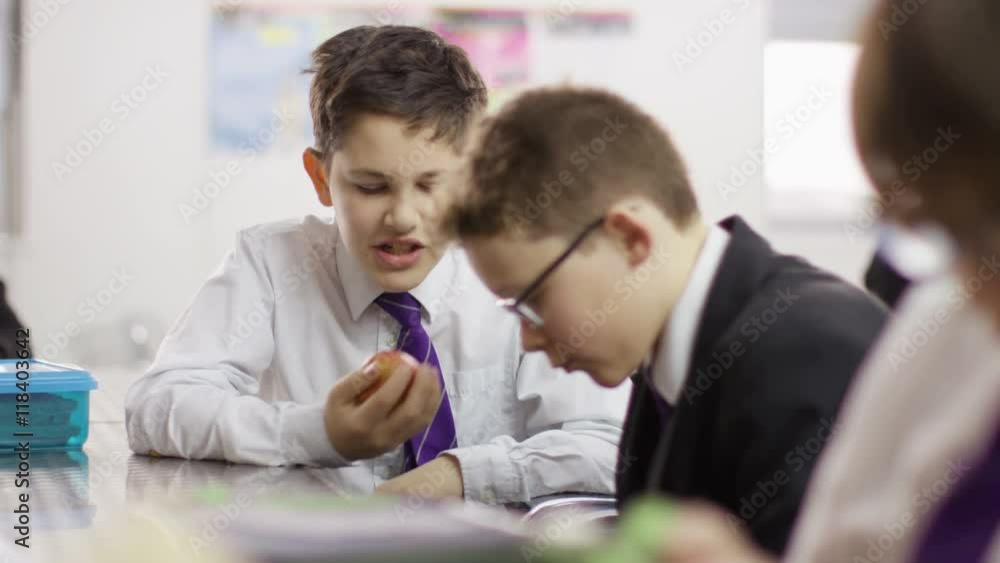 Young boy eating an apple in school cafeteria & talking to his friend Young boy eating an apple in school cafeteria & talking to his friend