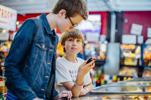 Caucasian brothers using cell phone in arcade photo