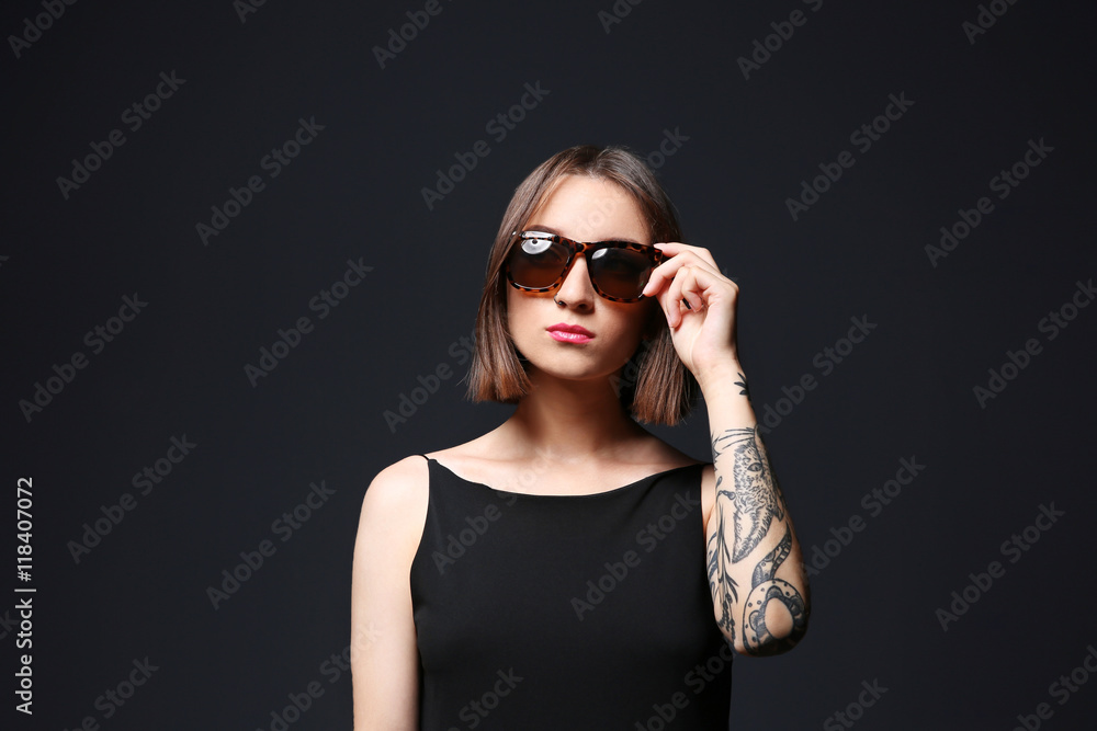 Beautiful young woman with tattoo wearing sunglasses and posing on black background Beautiful young woman with tattoo wearing sunglasses and posing on black background