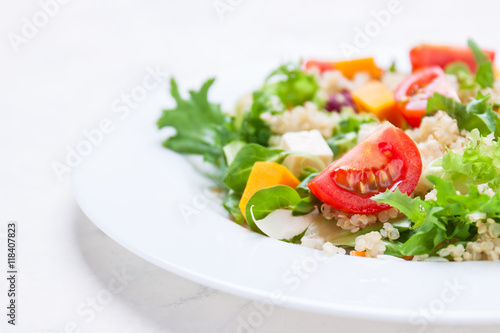 Homemade autumn healthy salad with quinoa, salad leaves, tomatoes, pumpkin and feta cheese on a white plate, closeup