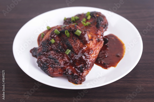 Grilled chicken or ayam golek on white plate, wooden background.