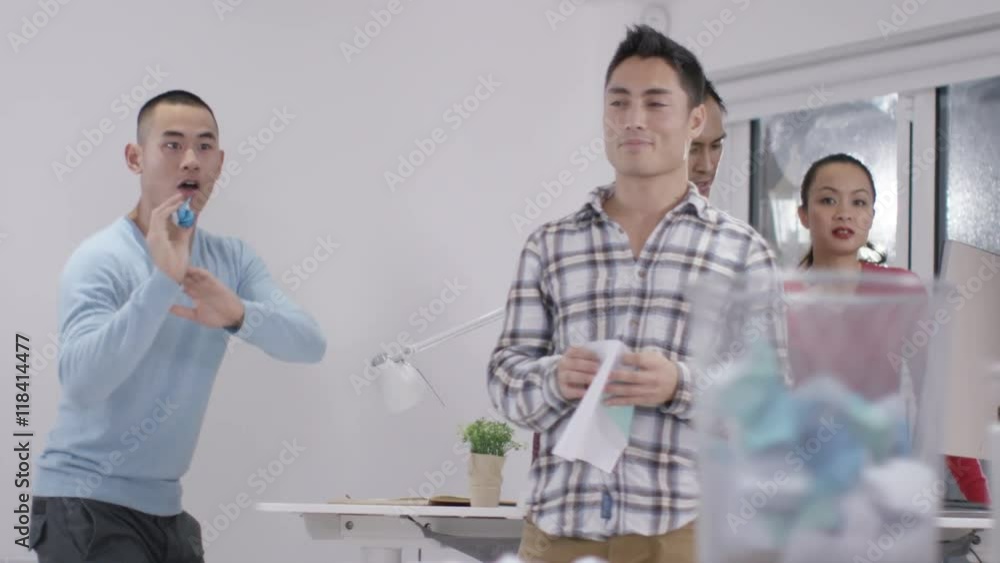 Casual office workers aiming rolled up papers for waste paper basket Casual office workers aiming rolled up papers for waste paper basket