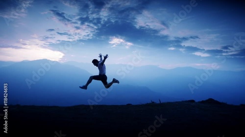 Silhouette of man jumping of happiness and success on the top of a mountain. Slow motion photo