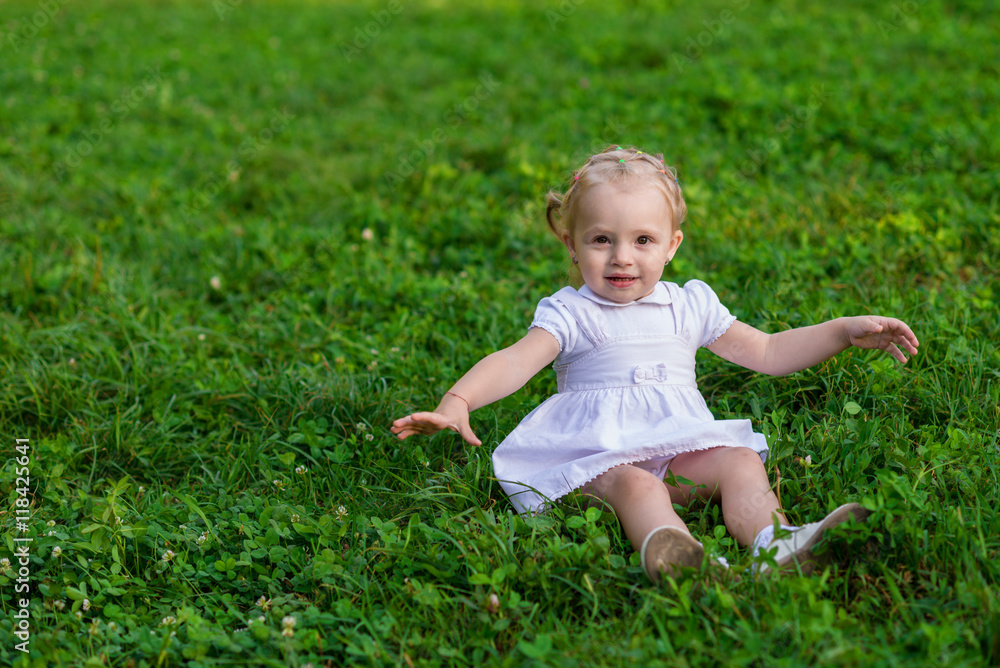 Baby girl in white dress sits and smiling on the fresh green grass Baby girl in white dress sits and smiling on the fresh green grass