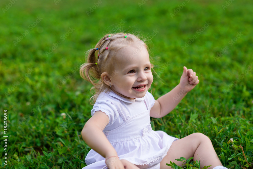 Baby girl in white dress sits and smiling on the fresh green grass Baby girl in white dress sits and smiling on the fresh green grass