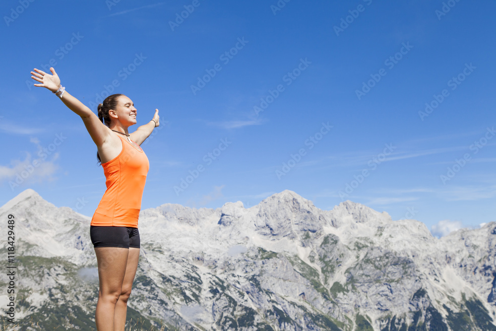 Young pretty smiling woman hiker standing on a rock with raised outstretched hands, high in the mountains, freedom and happiness, achievement in mountains Young pretty smiling woman hiker standing on a rock with raised outstretched hands, high in the mountains, freedom and happiness, achievement in mountains