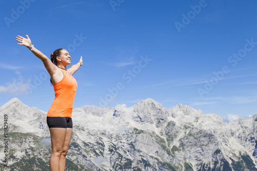 Young pretty smiling woman hiker standing on a rock with raised outstretched hands, high in the mountains, freedom and happiness, achievement in mountains 