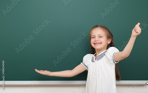 school student girl open arms at the clean blackboard, grimacing and emotions, dressed in a black suit, education concept, studio photo © soleg